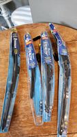 Four Michelin Stealth Hybrid beam wiper blades in partially opened blue packaging displayed on round wooden table.