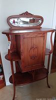 Front view showing oval mirror, top surface, central carved cabinet door, two curved side shelves and bottom shelf