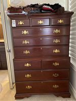 Front view of the Bernhardt high chest dresser showing all drawers with brass handles and a mahogany finish. Clothing placed on top, not included in sale.