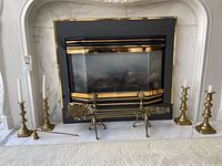 Front view of the fireplace with brass candlesticks, fireplace dogs, and fireplace tools arranged in front of it.