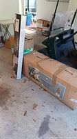 Photo of two large boxes in garage. One tall narrow box and one long rectangular box, containing Christmas decorations.