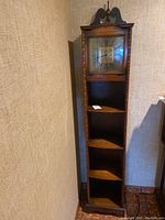 Full view of tall standing clock with shelves integrated below the clock face. Positioned in corner of room.