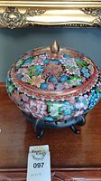 Front view of round cloisonné lidded enamel bowl with floral motifs and bronze finial on lid on wooden stand