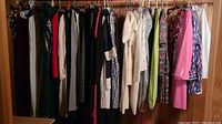 Wardrobe rack of assorted women's clothing including dresses, jackets, blouses in multiple colors and styles.