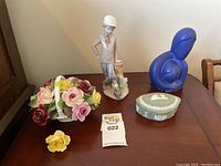 Photo showing all four items on a wooden table: Lladro Nao boy figurine, Wedgwood trinket box, Royal Adderley floral basket and blue resin figurine.