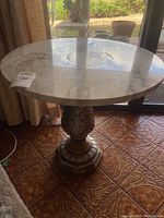 Side angle showing marble top and metal base with ornate floral and geometric detailing.
