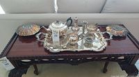 Tea service set displayed on wooden bench including large decorative tray, teapot, sugar bowl, creamer, two flower frogs, and candle holder
