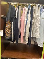 Women's clothing hung on a rod including sweaters, tops, vests, and jackets of various colors and styles
