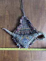 Front view of the triangular handmade talisman showing embroidery and tassels with attached hanging string.