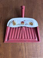 Front view of vintage metal dust pan with red handle, white top featuring painted coffee pot, coffee grinder, and teapot design.
