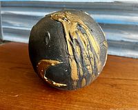 Close-up photo of the black spherical art piece showing gold dust streaks and textured surface, placed on a wooden surface.