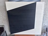 Front angle view of 3 ft by 3 ft square canvas painting showing abstract black quadrilateral shape on white background.