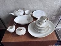 Full set arranged on wooden surface showing cups, saucers, plates, teapot, creamer, sugar bowl, and bowls with gold trim and floral designs
