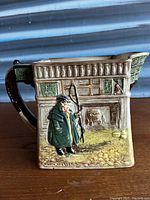 Front view of the Royal Doulton ceramic jug showing the inn facade and character Tony Weller in green coat holding a whip, with intricate architectural details.
