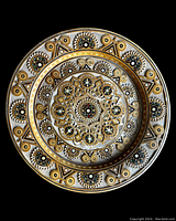Top view of the carved wooden plate showing intricate circular folk art patterns with floral and geometric shapes accented with gold, black, and white paint.