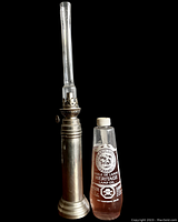 Front view of the vintage pewter oil lamp with accompanying bottle of Heritage lamp oil on a black background.