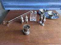 Photo showing all vintage kitchen items arranged on a wooden surface including pie plate piece, egg holder, milk and sugar vessels, and three pairs of salt and pepper shakers