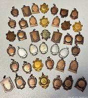 Top-down view of 28 assorted vintage Birks metal tags arranged in rows showing various shapes and metal finishes.
