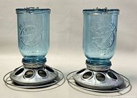 Photo of both Perky-Pet blue glass mason jar wild bird feeders side by side showing front logo and metal bases.