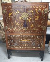 Front view of wooden antique Chinese hand painted cabinet showing decorative doors, ornamental metal hinges and central latch, and decorative lower drawer.