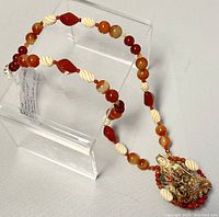 Full view of 20-inch carnelian bead necklace with off-white twisted beads and carved pendant shown on stand.