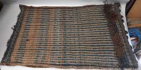 Full view of one Middle Eastern saddle bag rug, showing horizontal striped and zigzag pattern in muted blue and brown colors, some wear visible