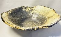 Close-up angled view of large oval pottery bowl with dark brown and yellow glaze and textured surface.