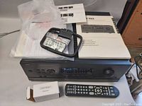 Receiver chassis on workbench with remote control, Audyssey microphone in box, user manual and plastic bag of accessories on top