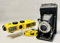 Minolta Weathermatic film camera and Kodak Vigilant Six 20 folding camera side by side on display stand