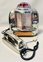 Front and side view of Venturer CR-9R jukebox style radio with coin slot mechanism and song selection buttons accompanied by RadioShack chrome wall mount phone handset in front.