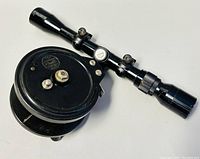 Rifle scope mounted on the fishing reel, showing the full length of the scope and reel body.