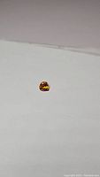 Photo showing the small, heart-shaped deep golden citrine gemstone on a white surface, highlighting its size, color, and cut.