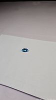 Photo of deep lagoon blue marquis cut Swiss blue topaz gemstone lying on white paper background showing color and shape.
