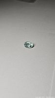 Oval cut aquamarine gemstone displayed on neutral background showing color and clarity.