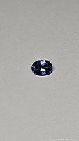 Oval faceted tanzanite gemstone on neutral background, showing color and cut