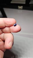 Photo showing the deep blue-purple oval faceted sapphire held between fingers, highlighting its size and shape.