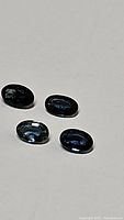 Four natural oval cut sapphires of mixed blue-green color placed on a light background.