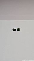 Two oval faceted deep green chrome diopside gemstones placed on flat white surface, front view showing shape and color.