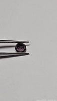 Natural electric purple spinel gemstone being held by tweezers showing cushion cut and electric purple color.
