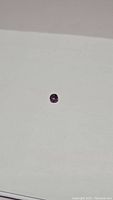 Photo showing round cut, purple untreated spinel gemstone on white background with clear facets and VS clarity.