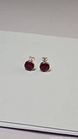 Pair of small red ruby stud earrings in sterling silver laid on white paper