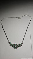 Necklace laid flat showing the cluster design of green emeralds and purple garnets on a silver chain.