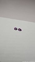 Pair of small purple pear-shaped amethyst gemstones on a plain white background, showing overall color and size matching