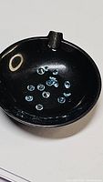 14 small round brilliant cut Paraiba blue apatite gemstones displayed in a black dish.