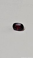 Photo showing close-up view of deep red cushion cut spinel gemstone on white background.