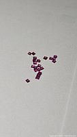 Close-up photo of 21 small, square-cut rubies in deep red color on a white surface, showing their clarity and untreated natural state.