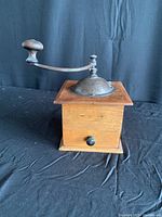 Front view of antique wooden pepper mill with metal crank and dome grinder.
