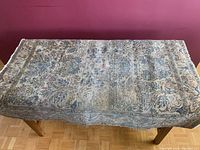 Full view of the rectangular antique oriental rug draped over a table, showing overall design and heavy dirtiness.