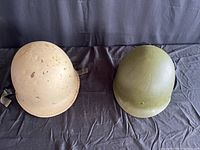 Two American helmets side by side, one tan with wear, one olive green, both with chin straps.