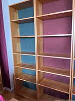 Photo of two tall wooden book shelves side by side against a wall, showing multiple shelves on each unit and their natural wood finish.